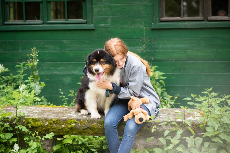 Frau sitzt mit einem Hund draußen lächelnd