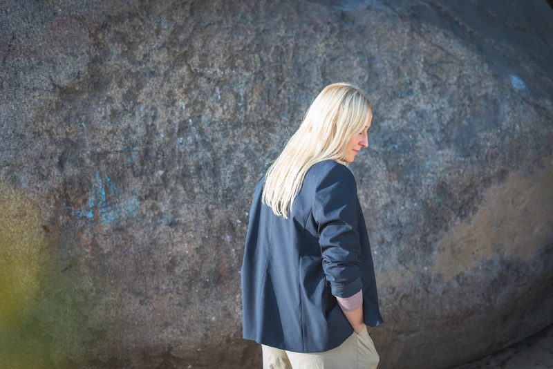Frau steht vor einer Steinwand mit dem Rücken zur Kamera