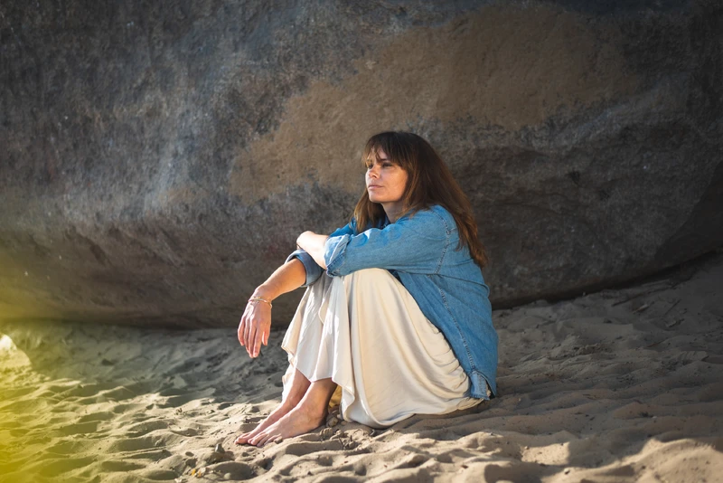 Frau sitzt am strand auf dem sand neben einer stein wand